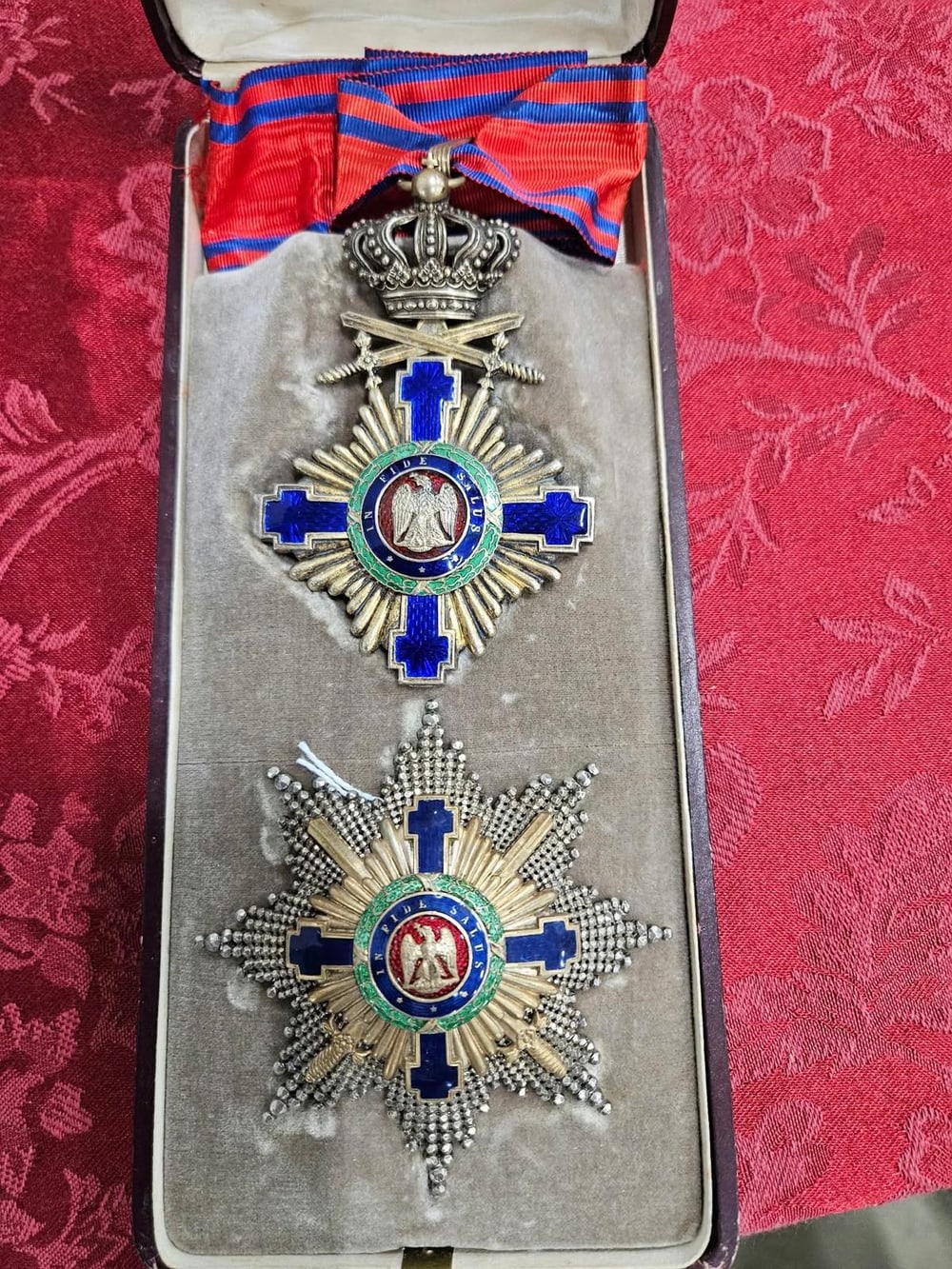 Orden de la Estrella de Rumanía con espadas: la cruz de cuello bajo la corona real y la placa con el lema «In fide salus», en su estuche con la cinta.