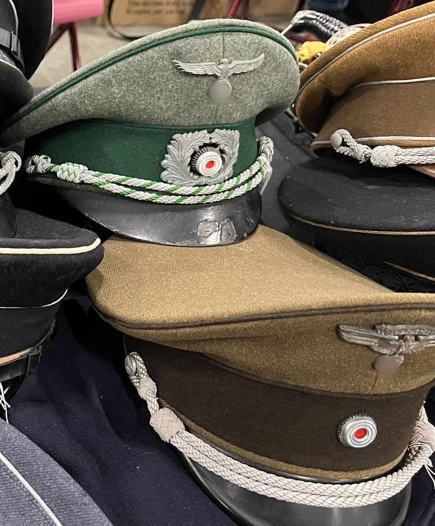 Gorras de visera de oficial, con el cordón trenzado de plata, la corona de roble y la escarapela. Los símbolos van tapados (§ 86a StGB).
